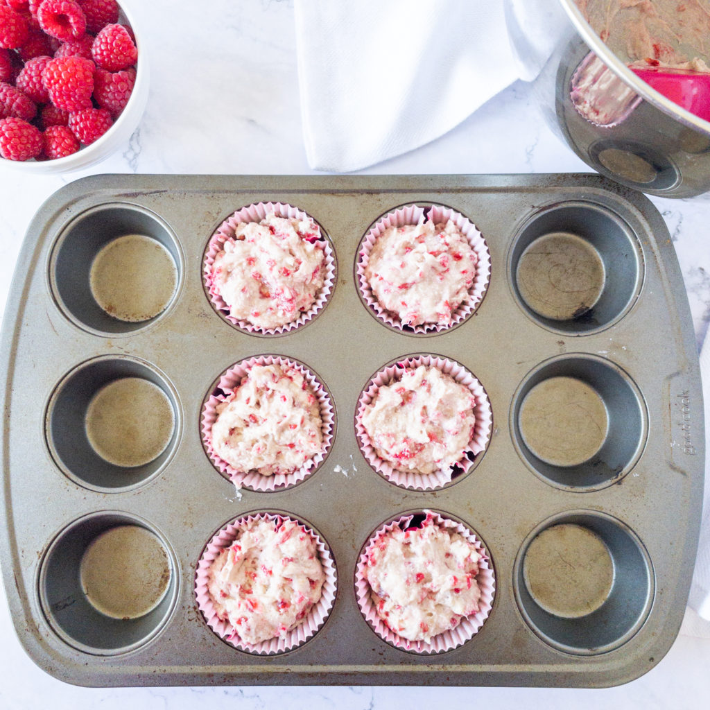 lined muffin pan filled with raspberry cupcake batter
