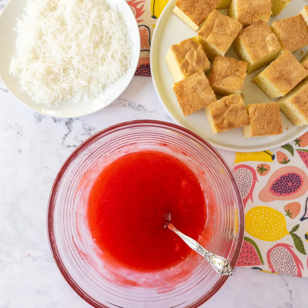 Semi-set jello in bowl with squares of sponge cake and shredded coconut in background