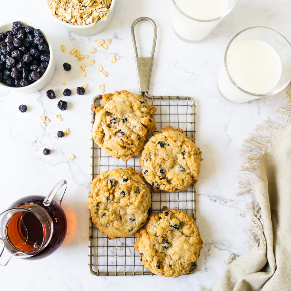 cookies on wire rack with a bowl of oats and blueberries and glasses of milk