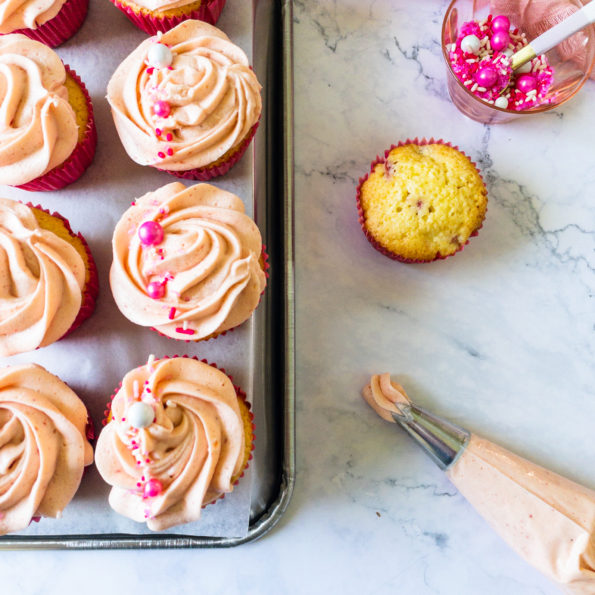 line of frosted cupcakes with piping bag and sprinkles to the side