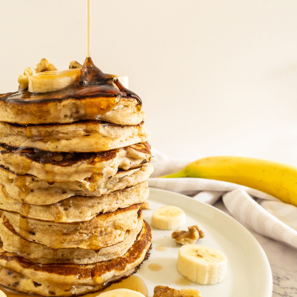 banana walnut pancake stack with maple syrup poured over top