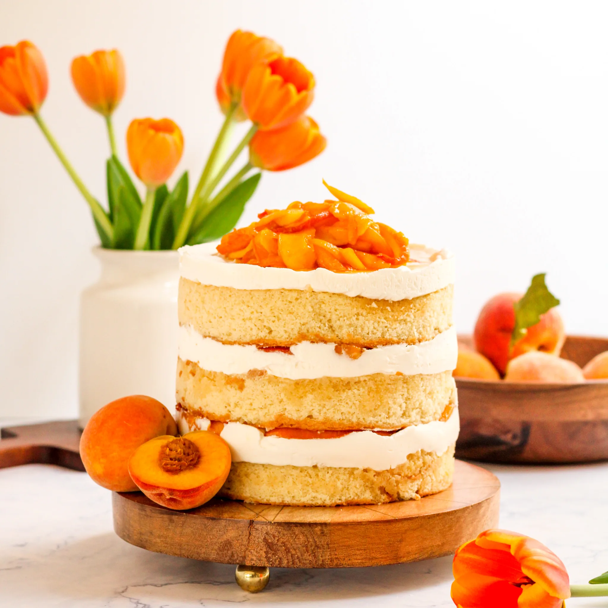 Whole peaches and cream layer cake on wooden stand